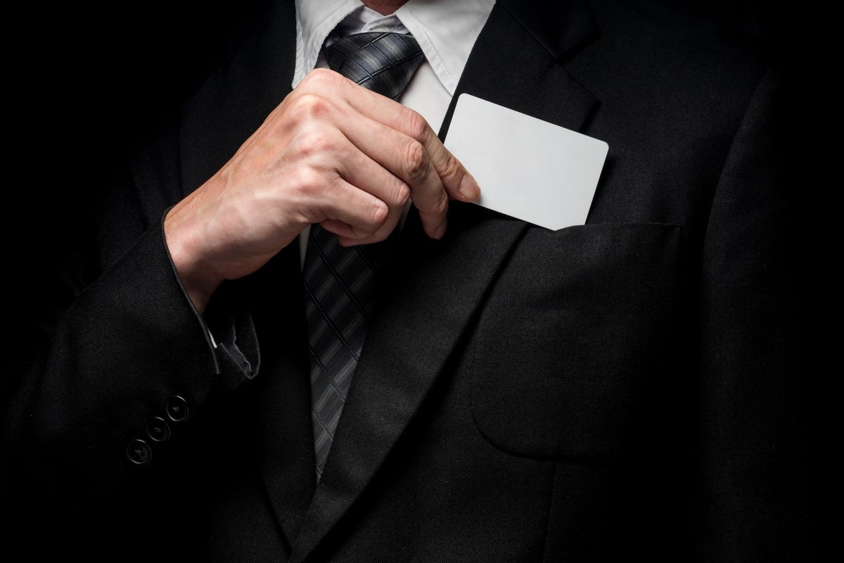 Close up of man in black suit holding business card on black background